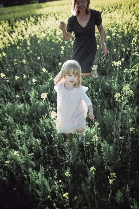 Portrait of little girl walking on rape field with her mother