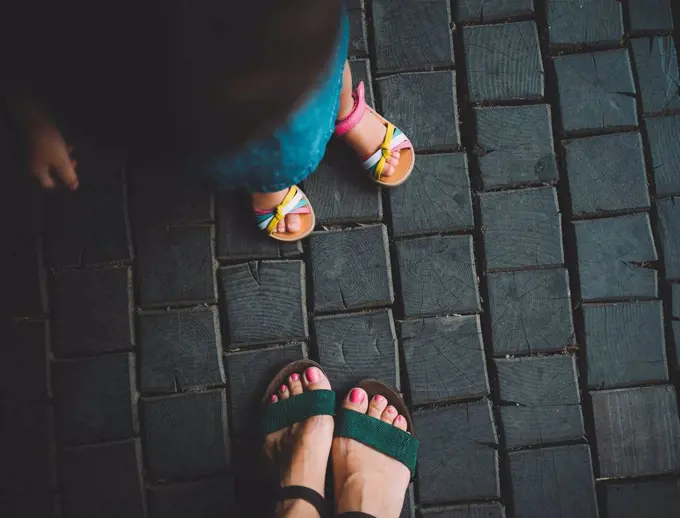 Feet of baby girl and her mother standing on wooden pavement, top view