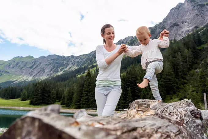 Germany, Bavaria, Oberstdorf, mother helping little daughter balancing on a log