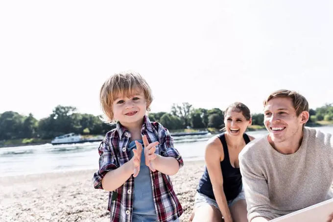 Happy boy clapping hands at the riverside with watching parents