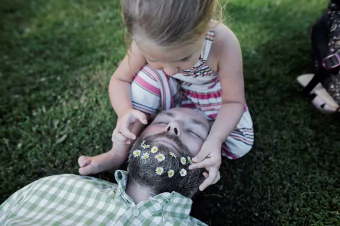 Little girl decorating father's beard with daisies on meadow in the garden