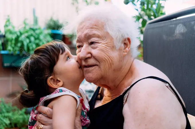 Baby girl kissing her grandmother on terrace