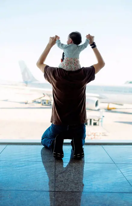 Man carrying a baby girl on his shoulders at the airport and looking at the airplanes, rear view