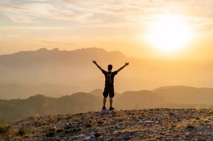 Spain, Barcelona, Natural Park of Sant Llorenc, man hiking and cheering at sunset