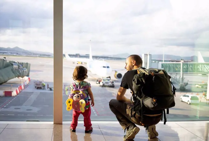 Father and daughter with backpacks at the airport looking at the planes