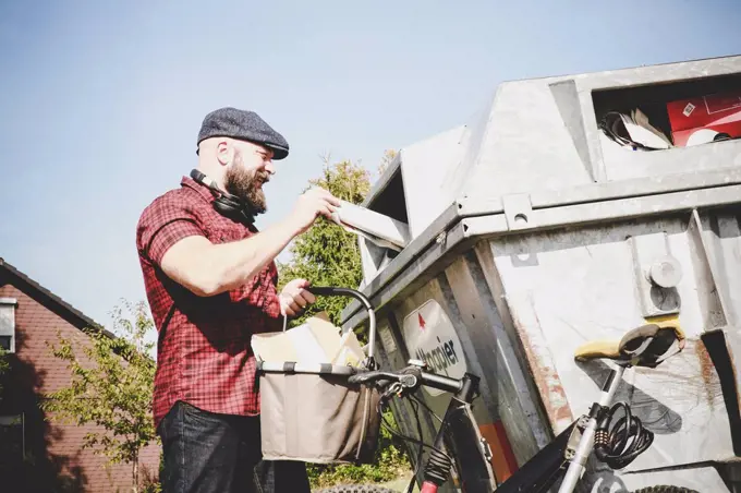 Cyclist recycling waste paper in paper bank