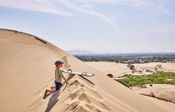 Peru, Ica, boy with sandboard on sand dune