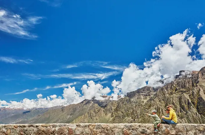 Peru, Chivay, Colca Canyon, woman sitting with sons on wall looking at canyon