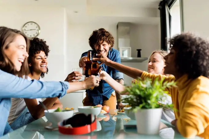 Cheerful friends clinking beer bottles at dining table