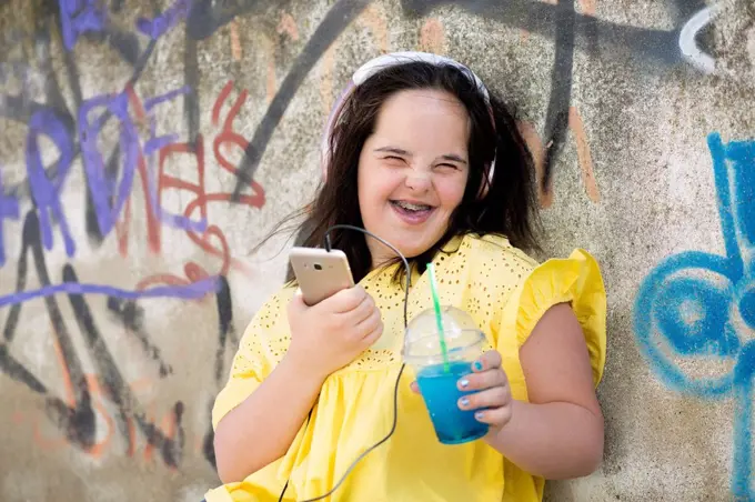 Teenager with down syndrome using smartphone, holding plastic cup