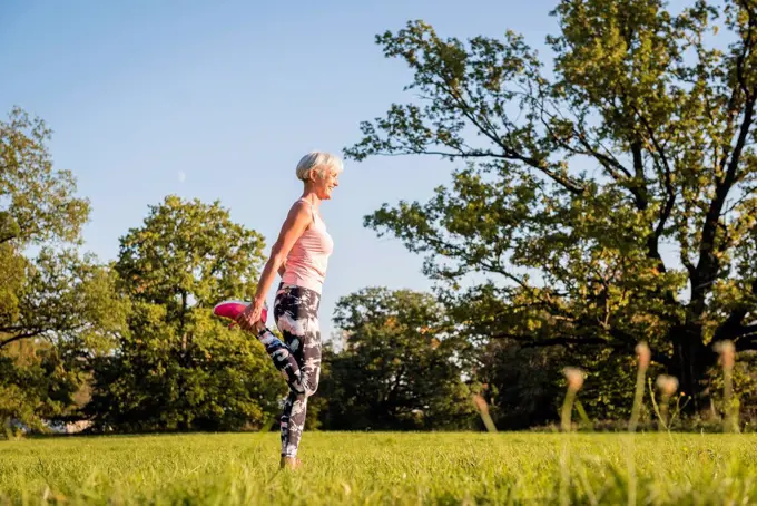 Senior woman stretching on rural meadow