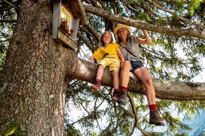 Portrait of smiling mother and daughter sitting in a tree