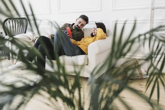 Couple sitting on the couch in the living room of new home looking at cell phone