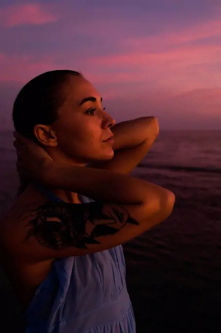 Profile of young woman with tattoo in front of the sea by sunset