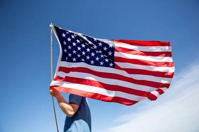 Man holding American flag under blue sky