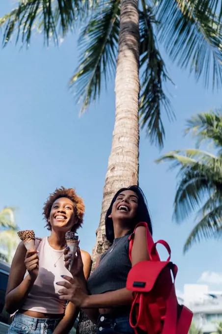 Two happy female friends with ice cream cones at a palm tree