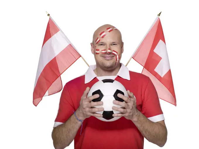 Man with Austrian flag painted on face, holding football, flags aside