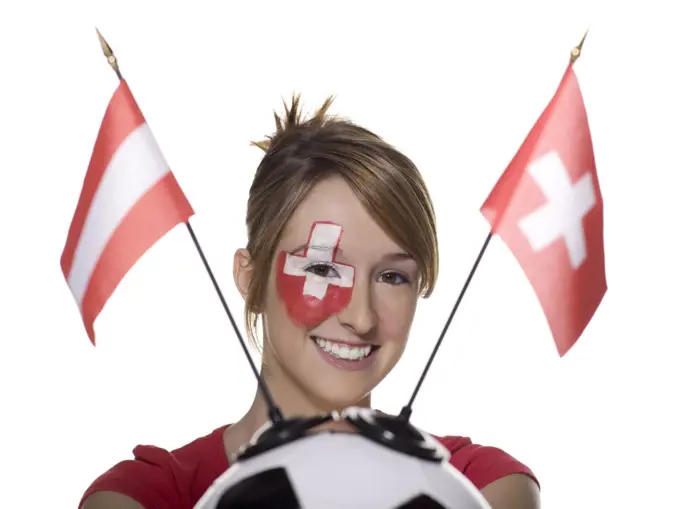 Woman with Swiss flag painted on face, holding football with flags