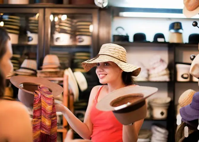 Croatia, Zagreb, Young women trying on hats in hat store