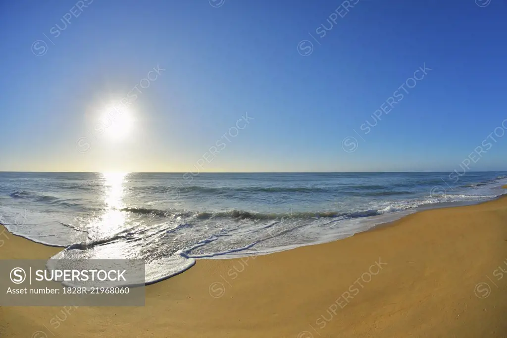 Surf breaking on the shoreline of Ninety Mile Beach at Paradise Beach with the sun shining over the ocean in Victoria, Australia