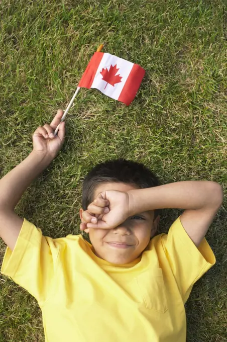 Portrait of Boy Lying on Grass, Holding Canadian Flag   