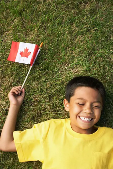 Portrait of Boy Lying on Grass, Holding Canadian Flag   