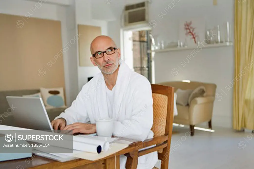 Mature man sitting at the dining table and working on a laptop