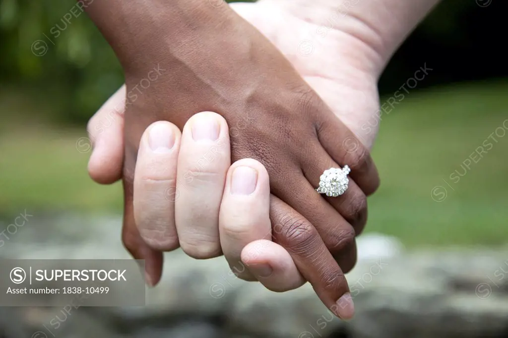 Interracial Couple Holding Hands and Diamond Engagement Ring, Close-Up