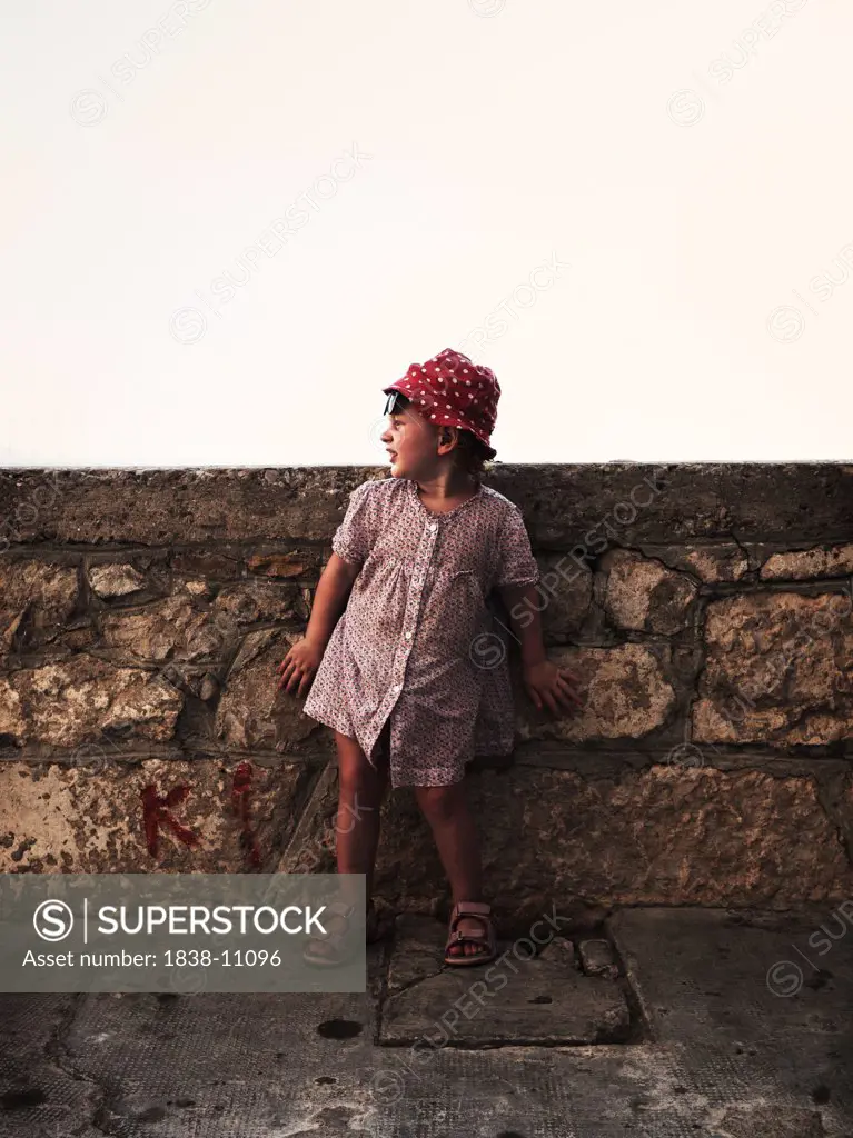 Young Girl in Red Hat and Print Dress Leaning Against Stone Wall, Croatia