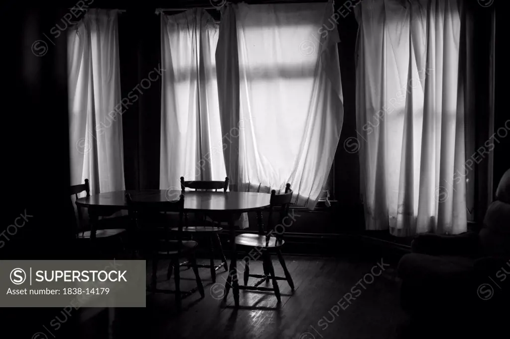 Dark Room With Drapes Covering Windows Behind Table and Chairs