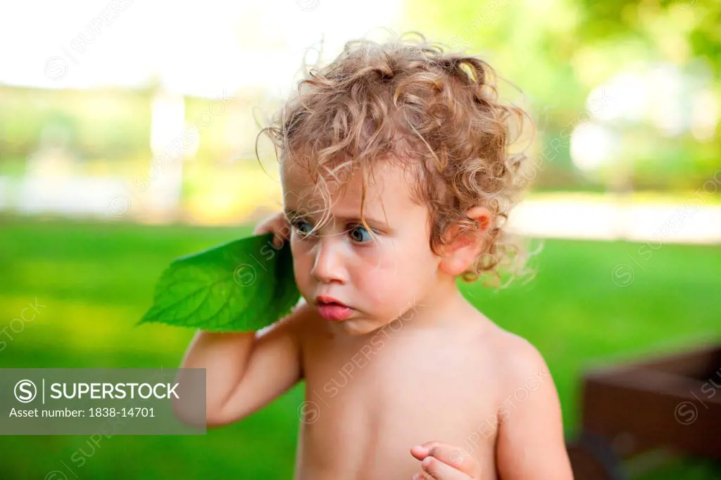 Young Shirtless Boy Listening to Green Leaf