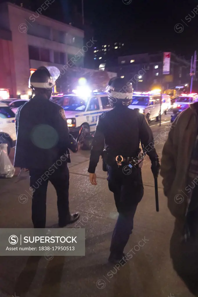 Rear View of Two Heavily Geared NYPD Officers walking with Helmets and Baton swinging, Lens Flare, Greenwich Village, New York City, New York, USA