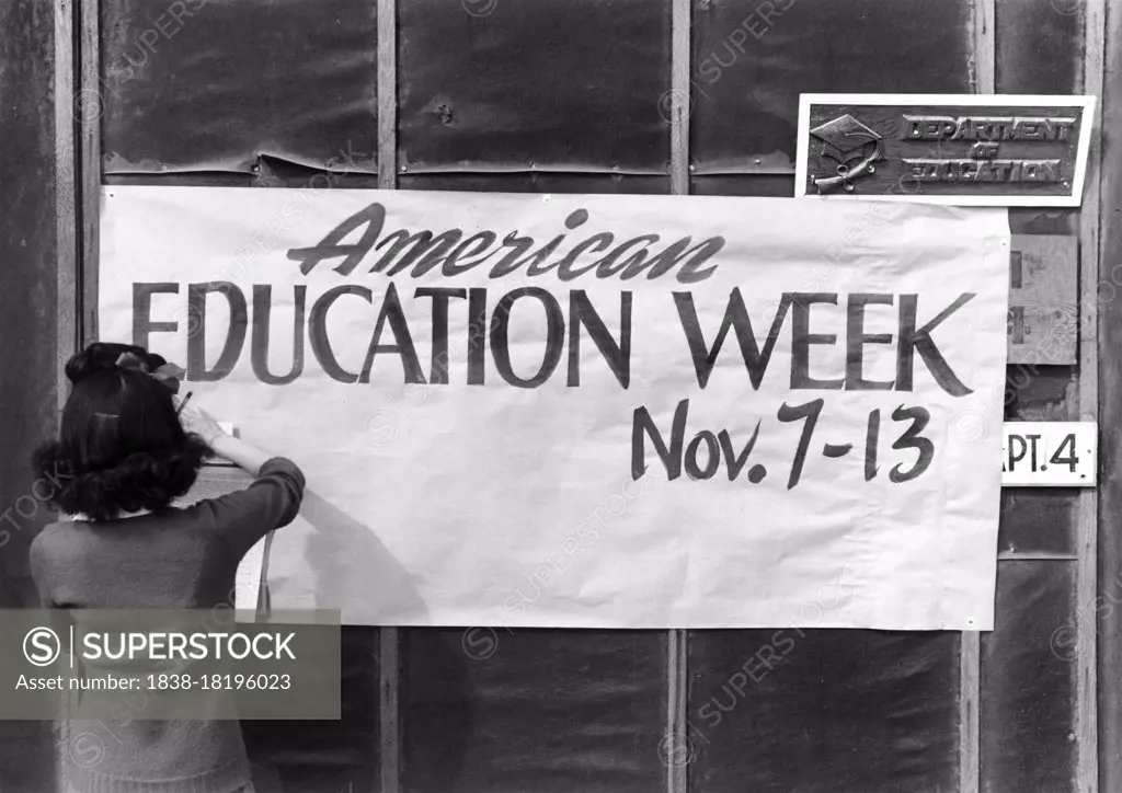 Woman hanging Sign promoting American Education Week to Wall of Education Department office, Manzanar Relocation Center, California, USA, Ansel Adams, Manzanar War Relocation Center Collection, 1943 