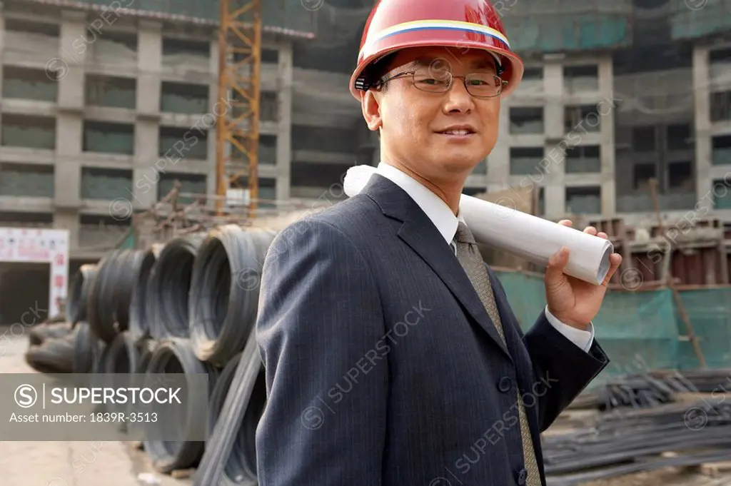 Businessman In A Construction Site Wearing A Hard Hat And Holding Plans