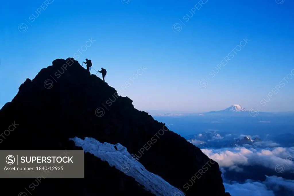 Two climbers approach summit of spire on Mount Rainer in Mount Rainier National Park, Washington. Mount Adams on the horizon.