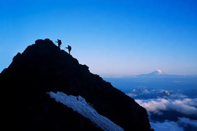 Two climbers approach summit of spire on Mount Rainer in Mount Rainier National Park, Washington. Mount Adams on the horizon.