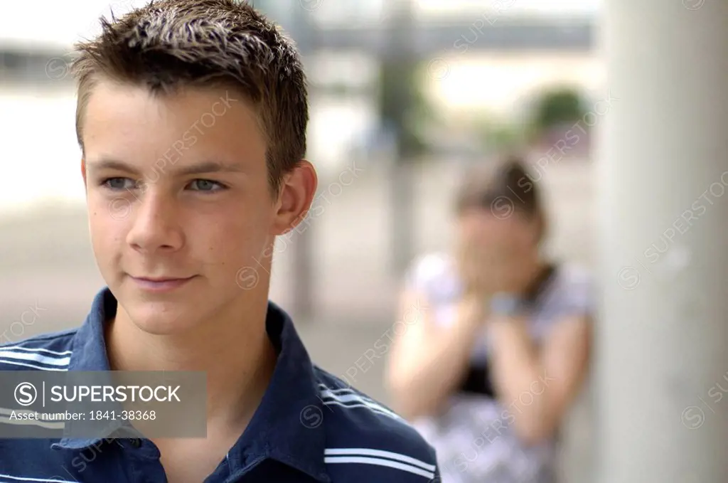 Close_up of teenage boy with his sobbing friend in background