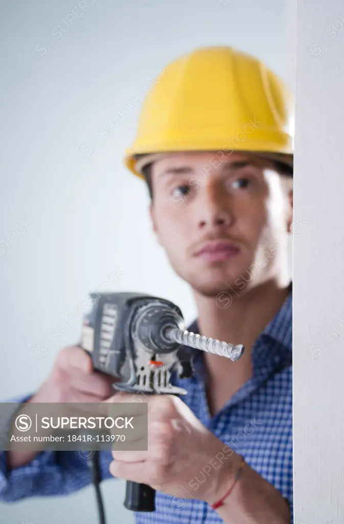 Young man wearing hard hat using drilling machine