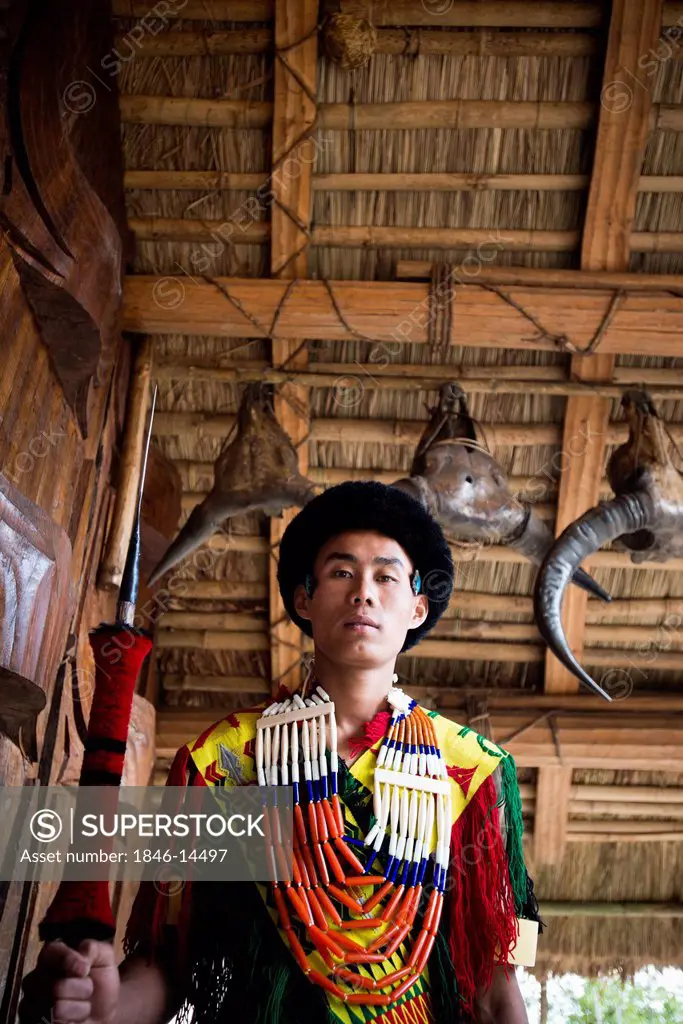 Naga tribal warrior in traditional outfit standing with spear in a hut, Hornbill Festival, Kohima, Nagaland, India