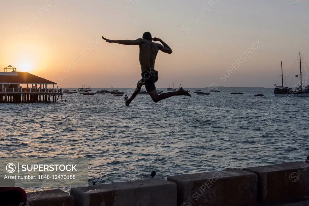 Young man jumping into the water, silhouette, at sunset, wharf, Zanzibar City, Zanzibar Archipelago, Tanzania