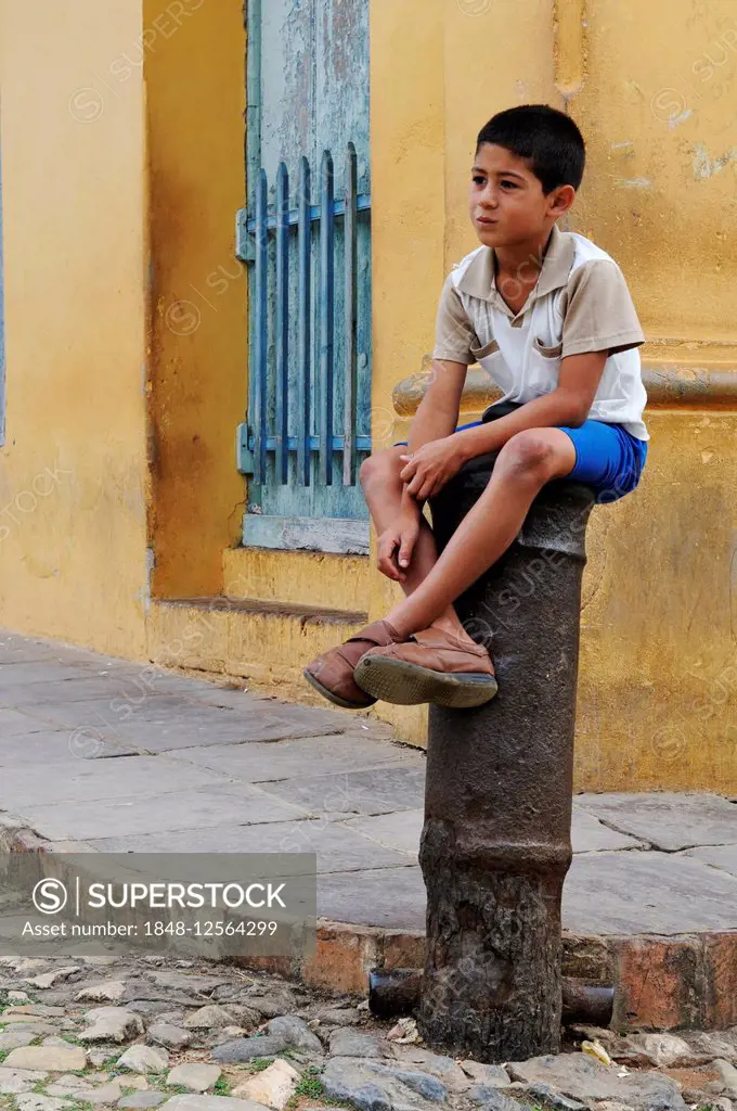 Boy sitting on a cannon, bollard in the historic centre of Trinidad, Sancti Spíritus Province, Cuba