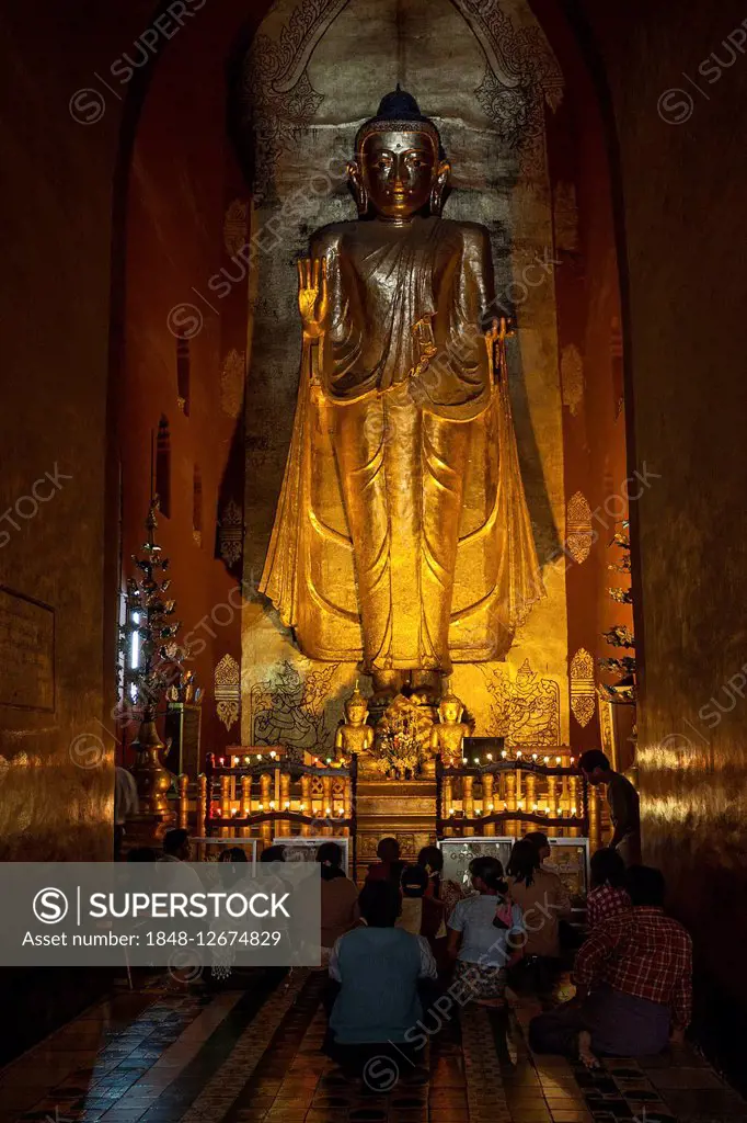 Standing gilded Buddha, Buddha statue, indigenous people sitting and praying, Ananda Temple, Bagan, Mandalay Division, Myanmar