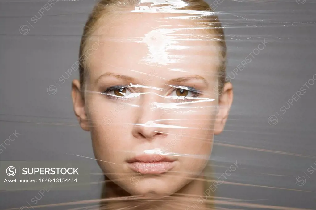 Young woman's face behind a sheet of clingfilm, symbolic for eternal youth