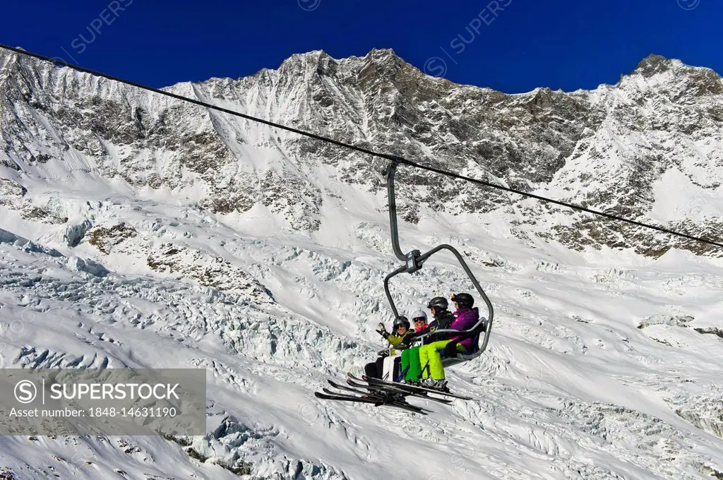 Skiers on a chairlift in front of the Feegletscher and the peaks Dom and Lenzspitze, Mischabel Group, Saas-Fee ski area, Valais, Switzerland