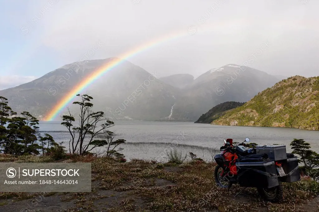 Heavily packed motorcycle in front of a lake behind a rainbow, O higgins, Region de Aysen, Chile