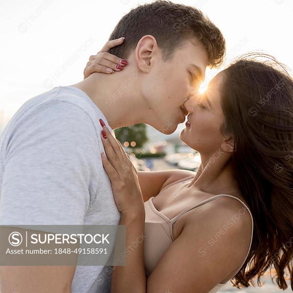 Side view couple kissing with sun peeking them - SuperStock