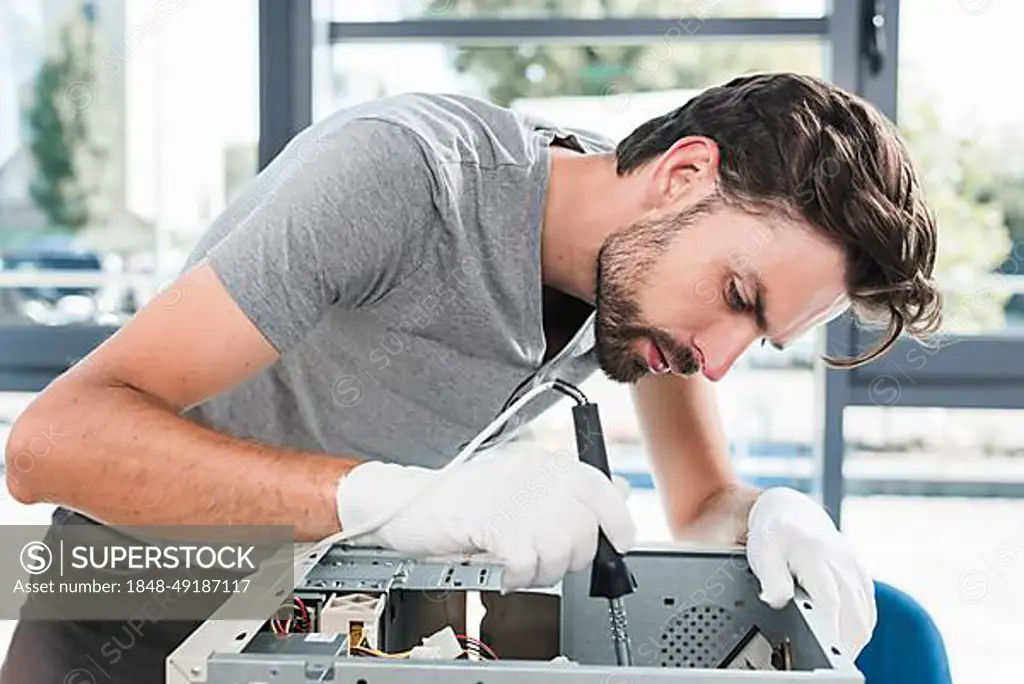 Side view young male technician working broken computer