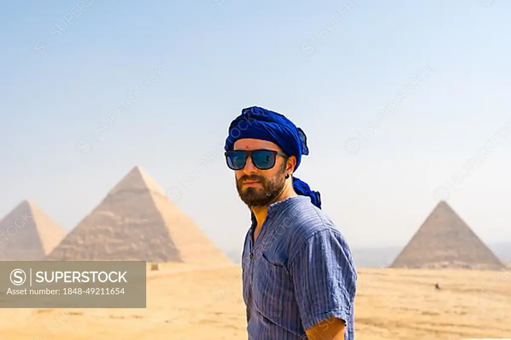 A young tourist wearing blue turban and sunglasses enjoying the Pyramids of Giza, the oldest Funerary monument in the world. In the city of Cairo, Egypt, Africa