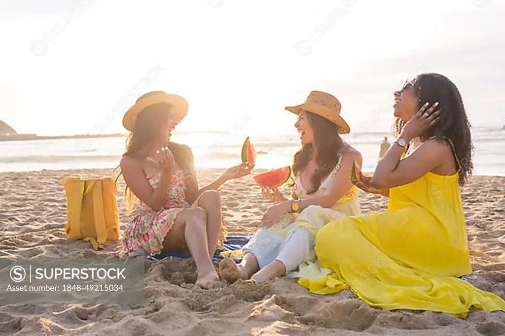 Friends eating healthy food during a picnic on the beach during sunset