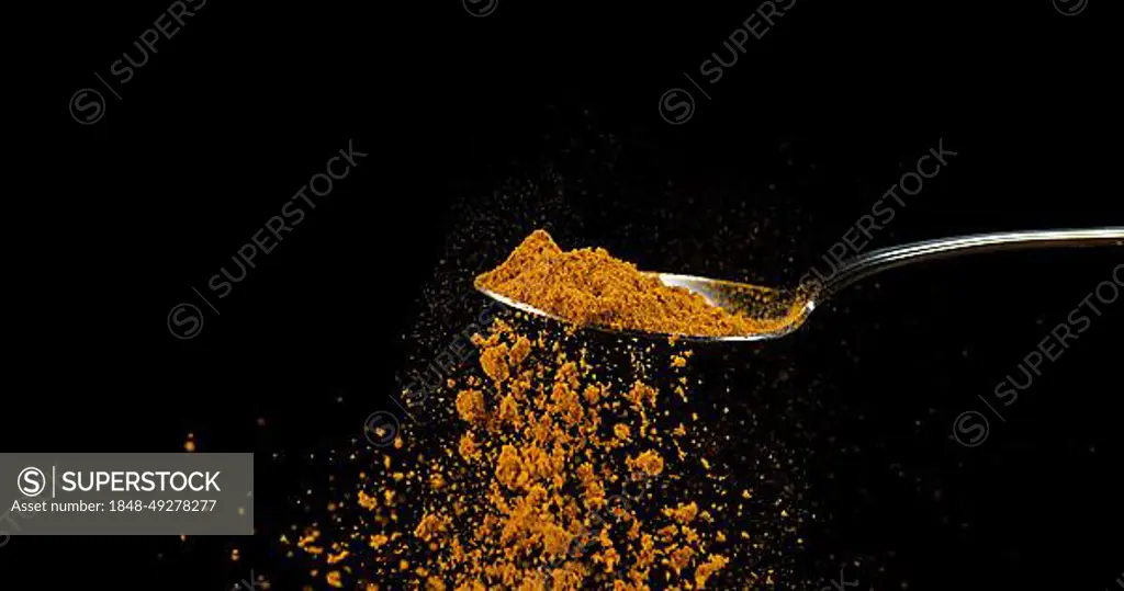 Spoon and Curry Powder falling from Spoon against Black Background